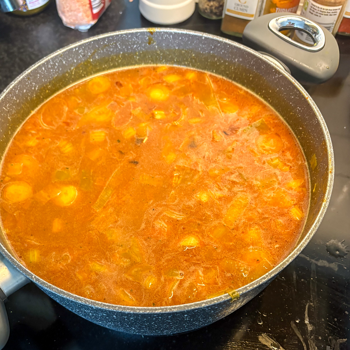 Pouring vegetable stock into the large pot over the red lentils and vegetables to begin simmering the healthy soup.