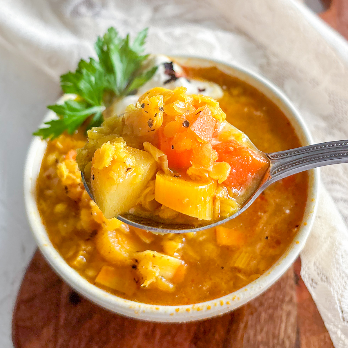 A spoonful of vibrant chunky spiced red lentil soup showing soft vegetables.