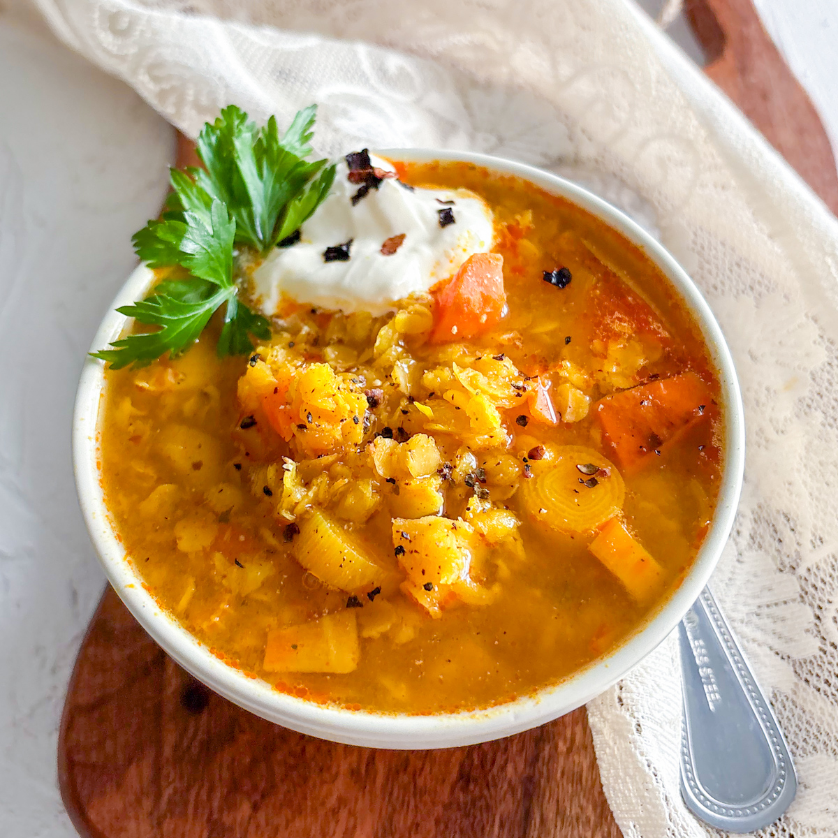 An overhead view of a rustic white bowl steaming with comforting, healthy lentil and vegetable soup