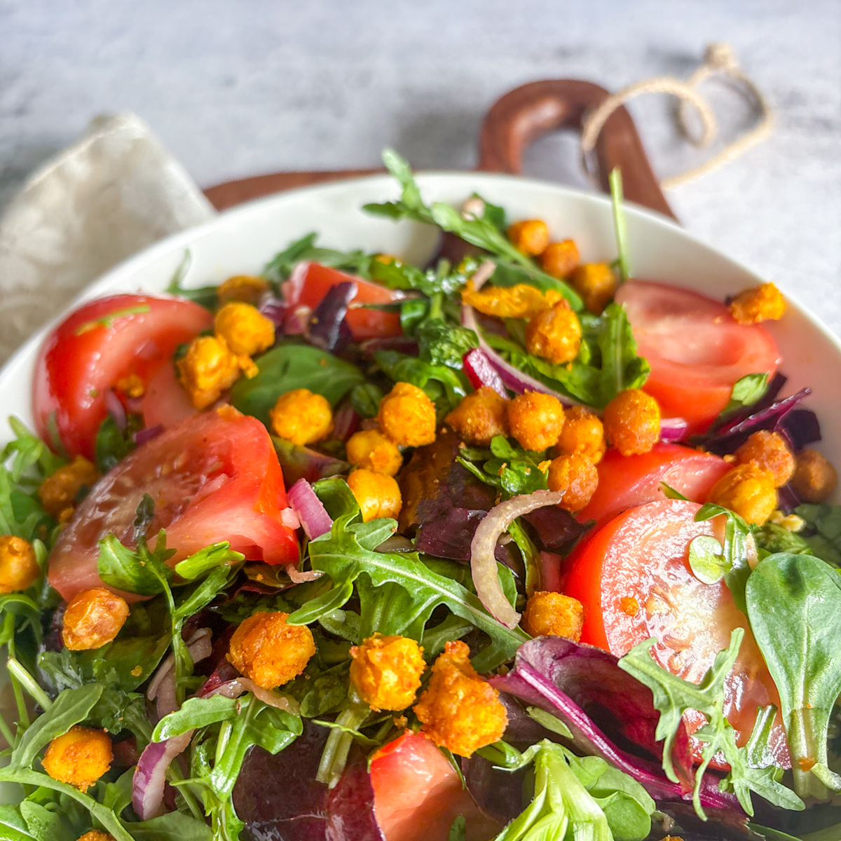 Close-up of a healthy leafy salad with fried chickpeas, fresh tomato wedges, and sliced red onion.