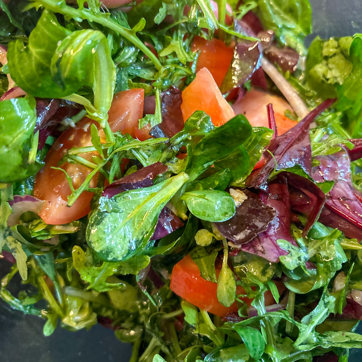 A focused close-up photograph showing a fork whisking a tangy balsamic vinaigrette, illustrating the blending of lemon juice, olive oil, and balsamic vinegar for a leafy chickpea salad.