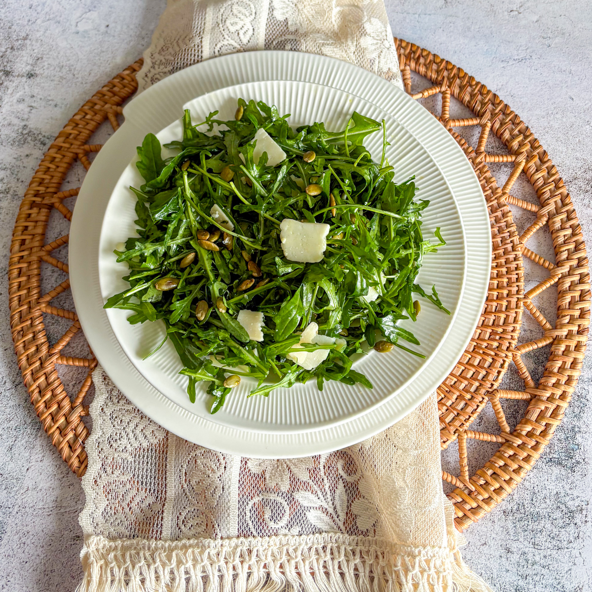 An easy rocket leaves salad recipe plated on a white dish, sitting on a woven mat and lace cloth.
