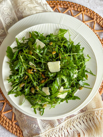 Fresh rocket and parmesan salad with toasted pumpkin seeds on a white plate, set on a rustic table setting.