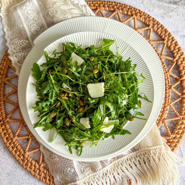 Fresh rocket and parmesan salad with toasted pumpkin seeds on a white plate, set on a rustic table setting.