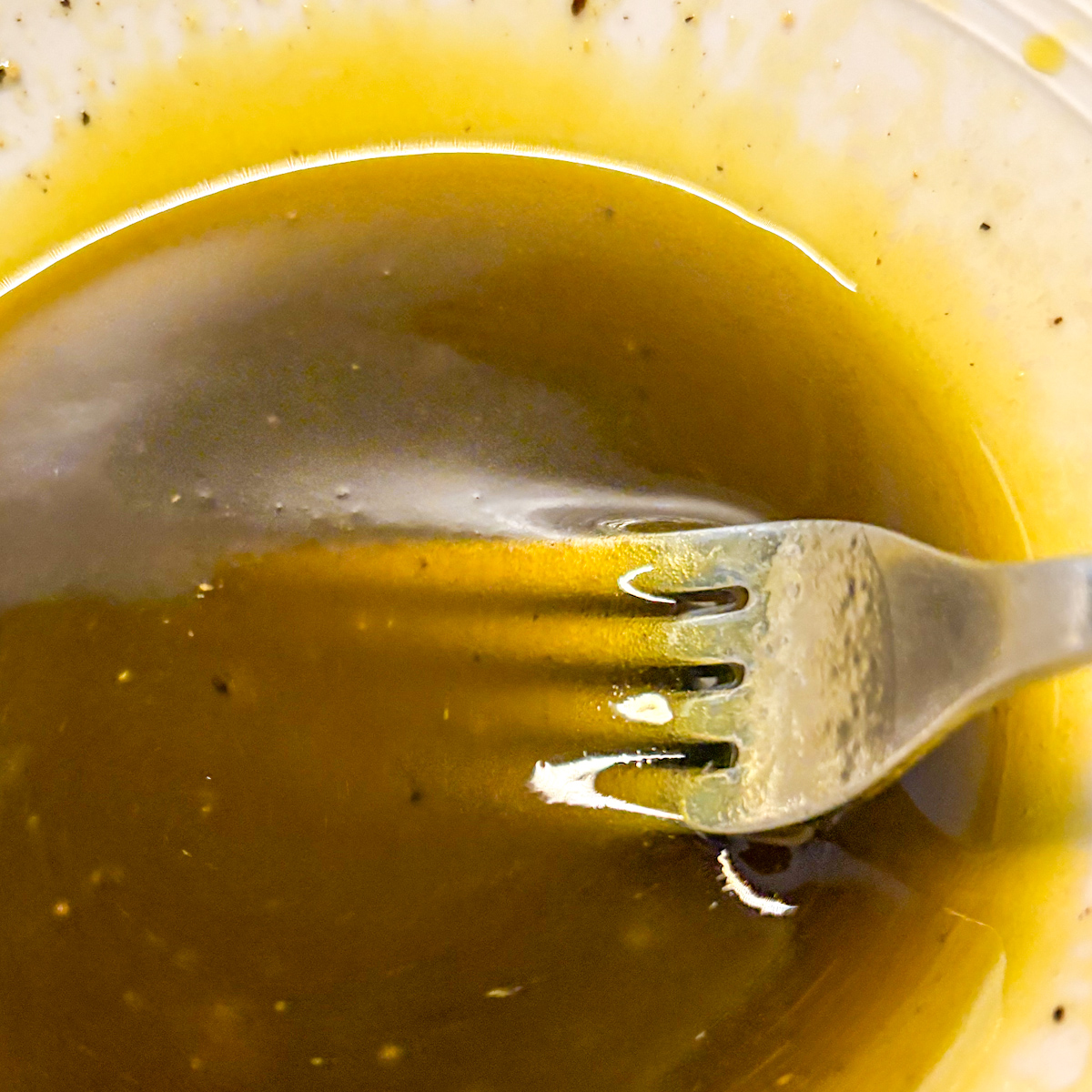 A fork whisking a quick rocket salad dressing made of olive oil, lemon juice, and balsamic vinegar in a small bowl.