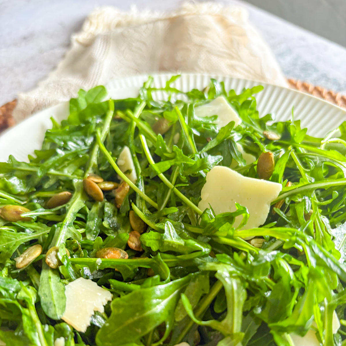 Close-up texture of fresh rocket leaves lightly coated in a tangy vinaigrette, mixed with toasted pumpkin seeds and parmesan pieces.