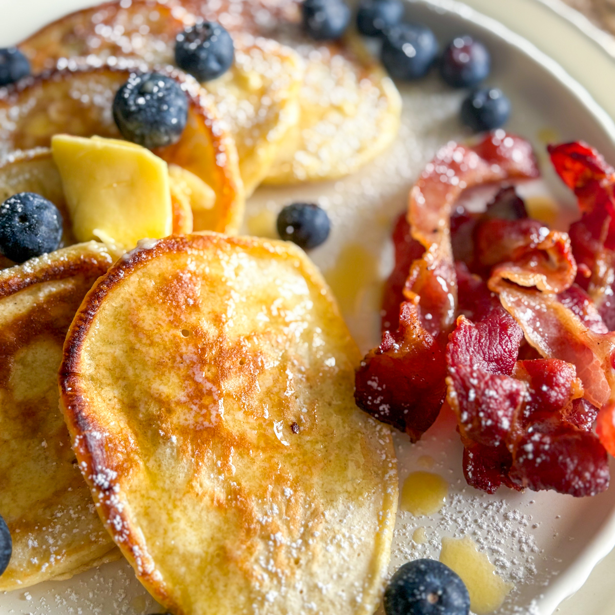 Close-up of mouth-watering, golden-brown thick pancakes topped with melting butter and blueberries for a comforting breakfast.