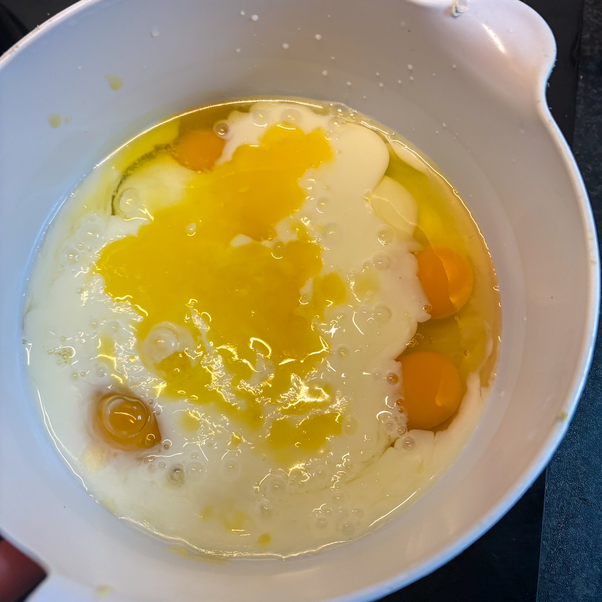 A whisk blending large eggs, vanilla essence, and room temperature buttermilk wet ingredients for the best buttermilk pancakes