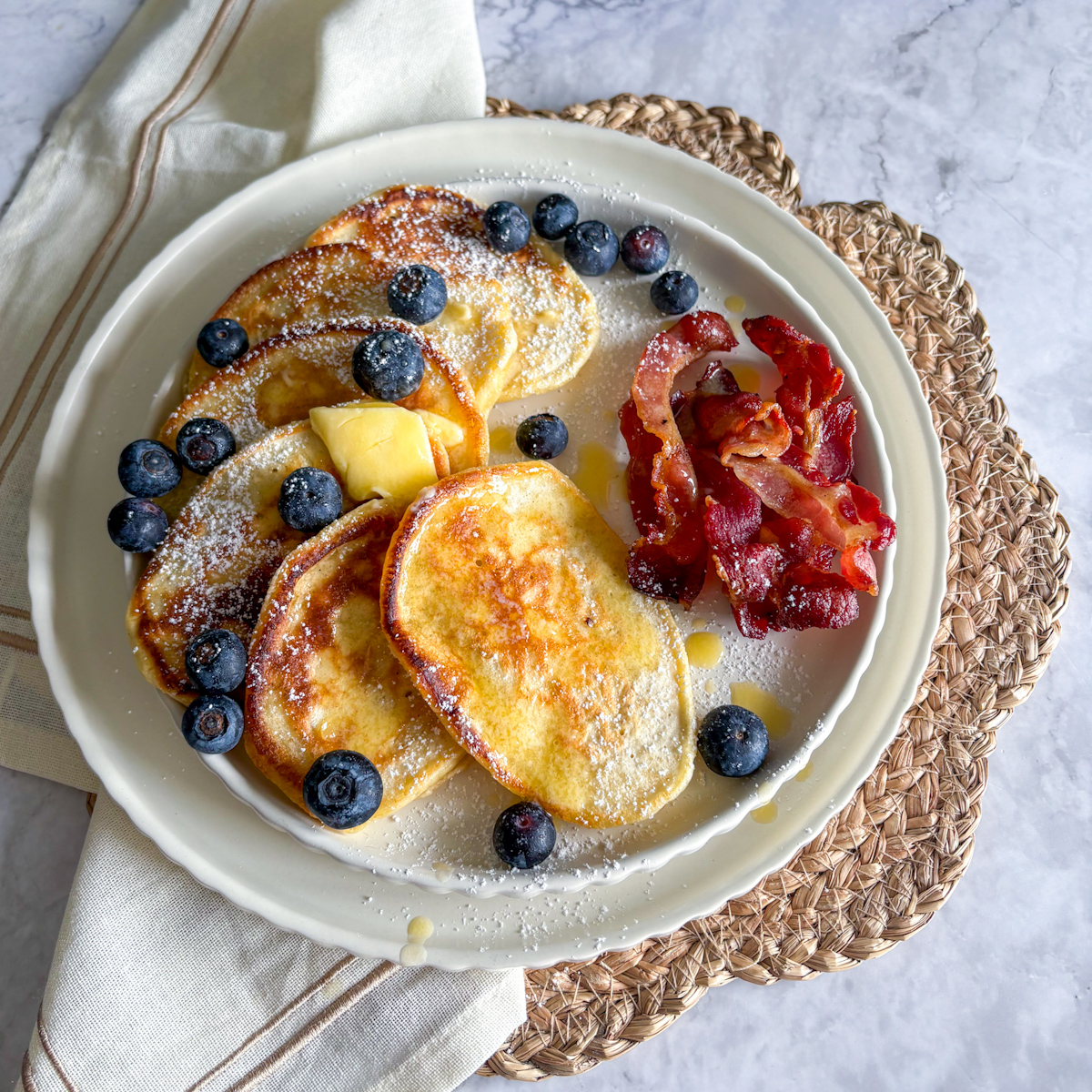 Fluffy Homemade Buttermilk Pancakes dusted with powdered sugar on a blue plate served with roasted bacon and fresh blueberries.