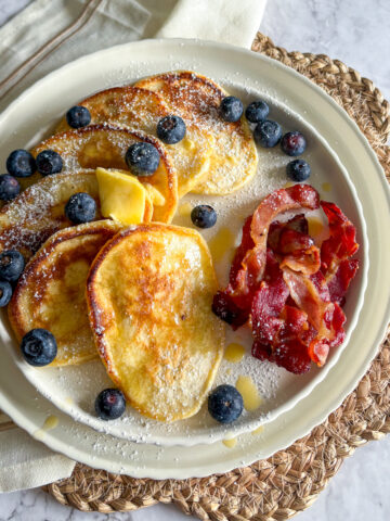 A sweet and savory breakfast plate featuring a stack of diner-style buttermilk pancakes, crispy bacon strips, and fresh blueberries.