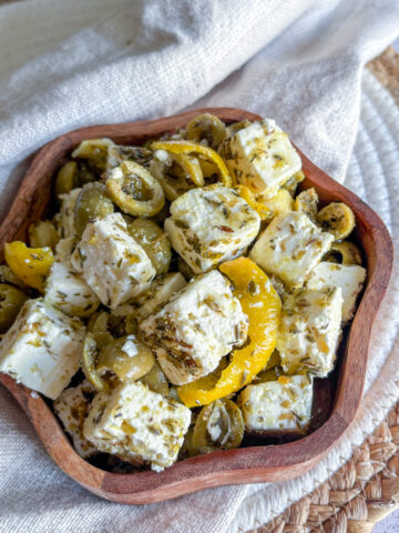 Marinated olives and feta in a wooden bowl with lemon peel and herbs