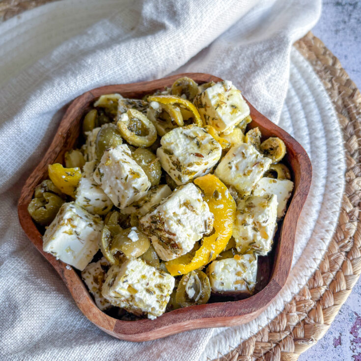 Marinated olives and feta in a wooden bowl with lemon peel and herbs