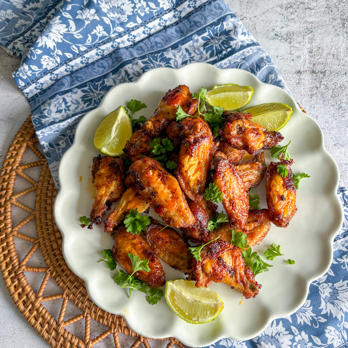  Golden pantry staples chicken wings served with lime wedges and parsley on a white plate.