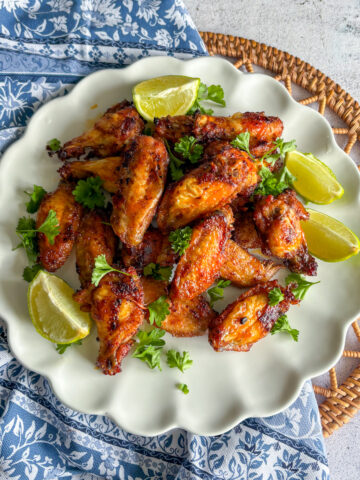 Pantry staples chicken wings on a white scalloped plate with lime wedges and fresh parsley.
