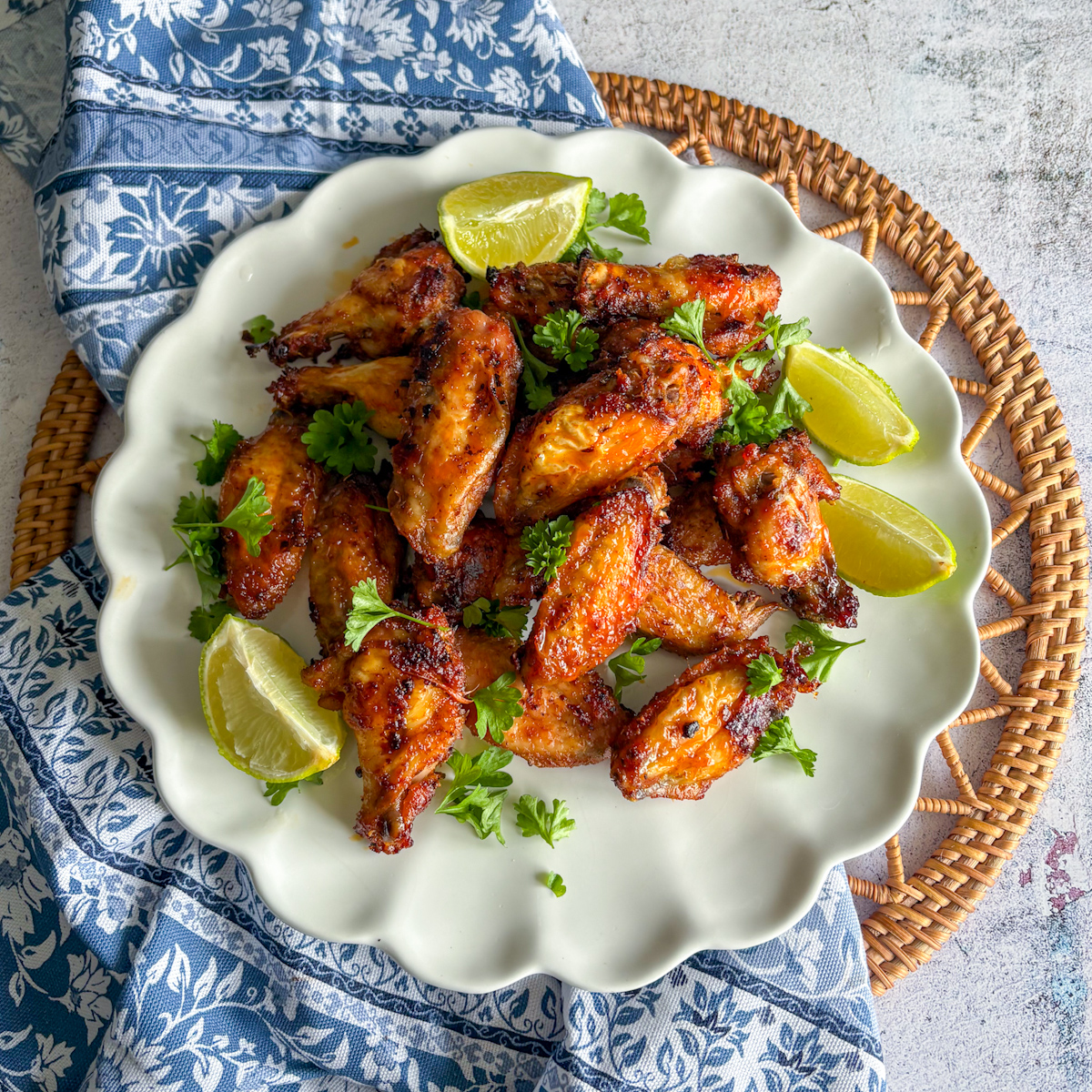 Pantry staples chicken wings on a white scalloped plate with lime wedges and fresh parsley.
