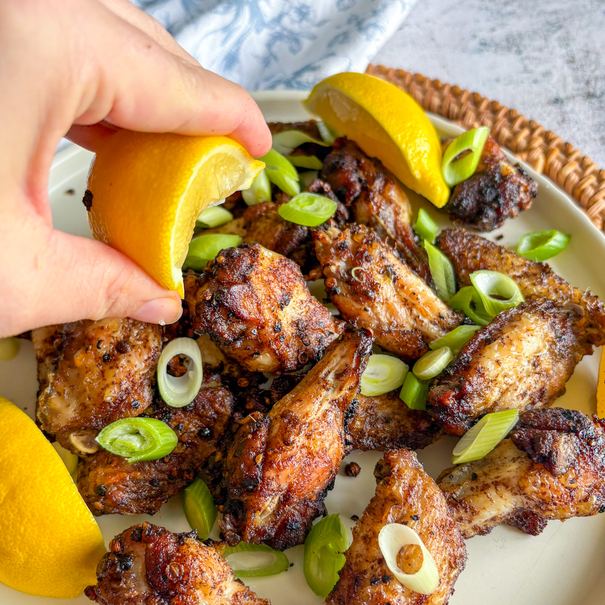 Hand squeezing fresh lemon over Crispy Peppercorn Coriander Chicken Wings with spring onions.