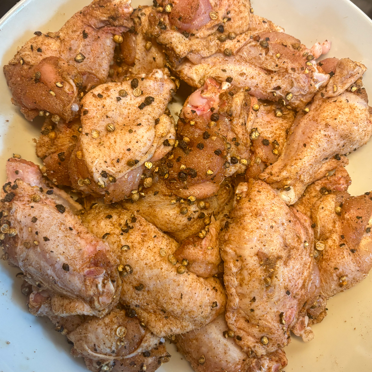 Raw chicken wings coated in smashed black peppercorn and coriander spice rub in a bowl.