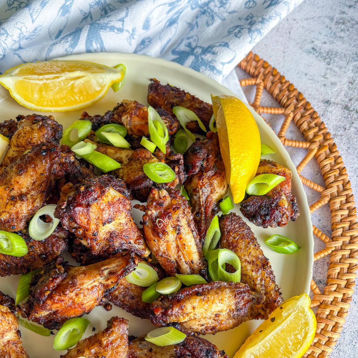 Crispy Peppercorn Coriander Chicken Wings plated with fresh lemon and spring onions on a wicker mat.