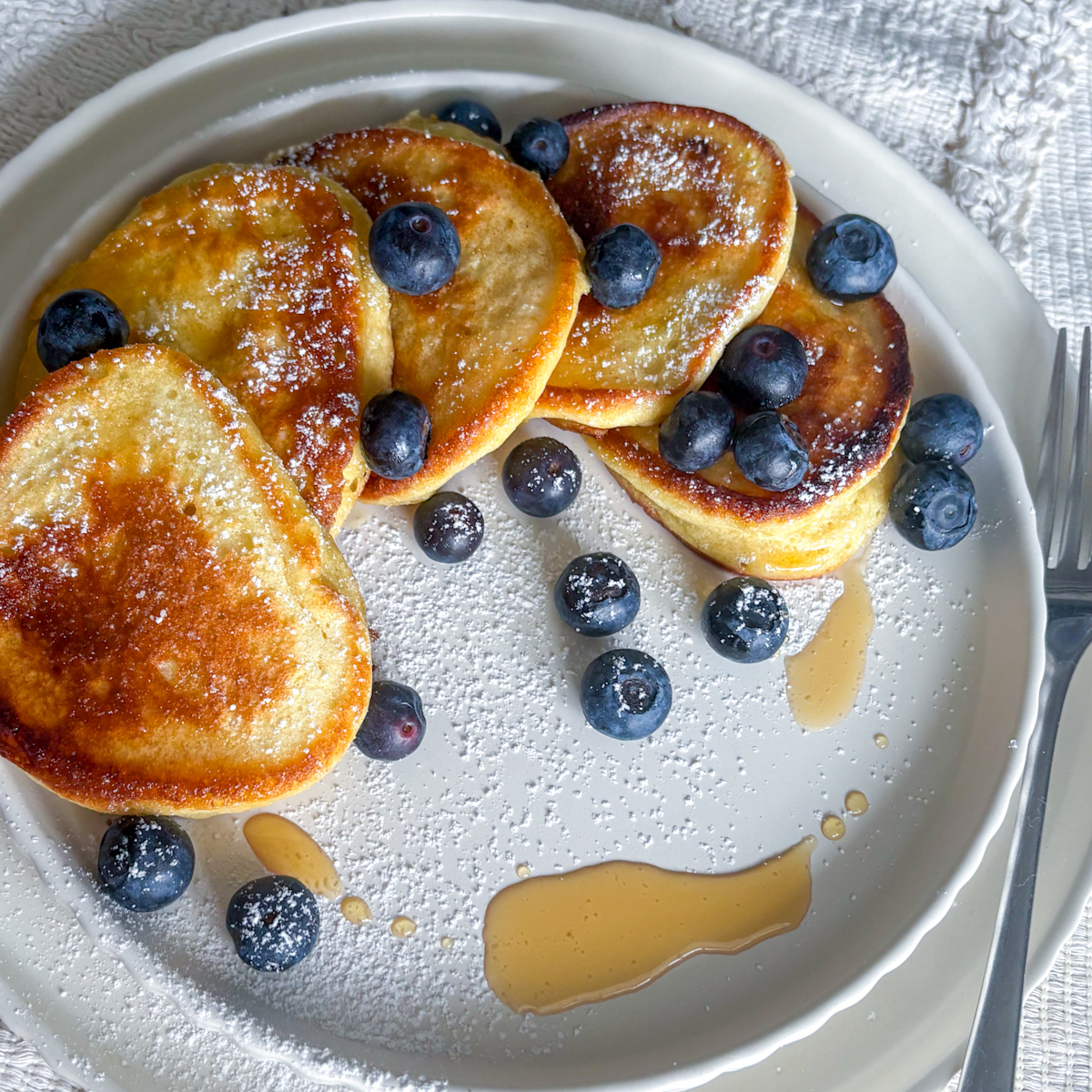 A plate of lemon ricotta pancakes dusted with icing sugar, showing the light and airy ricotta pancakes for brunch presentation.
