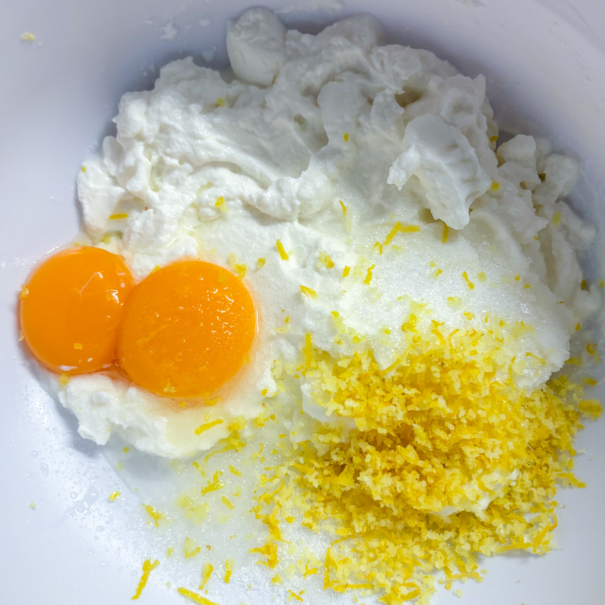 Mixing fresh ricotta cheese, milk, egg yolks, and lemon zest in a large glass bowl for ricotta pancakes.