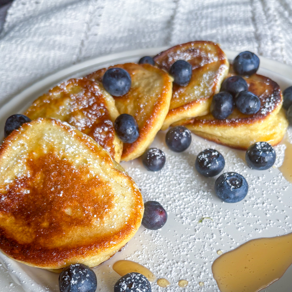 A close-up shot of fluffy ricotta pancakes with a golden-brown finish, served with fresh blueberries and a drizzle of syrup.