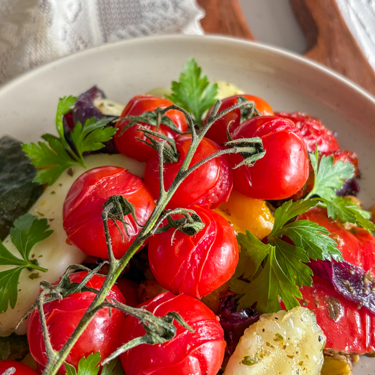 Close-up of juicy vine tomatoes resting on a colourful plate of roasted vegetables and halloumi.