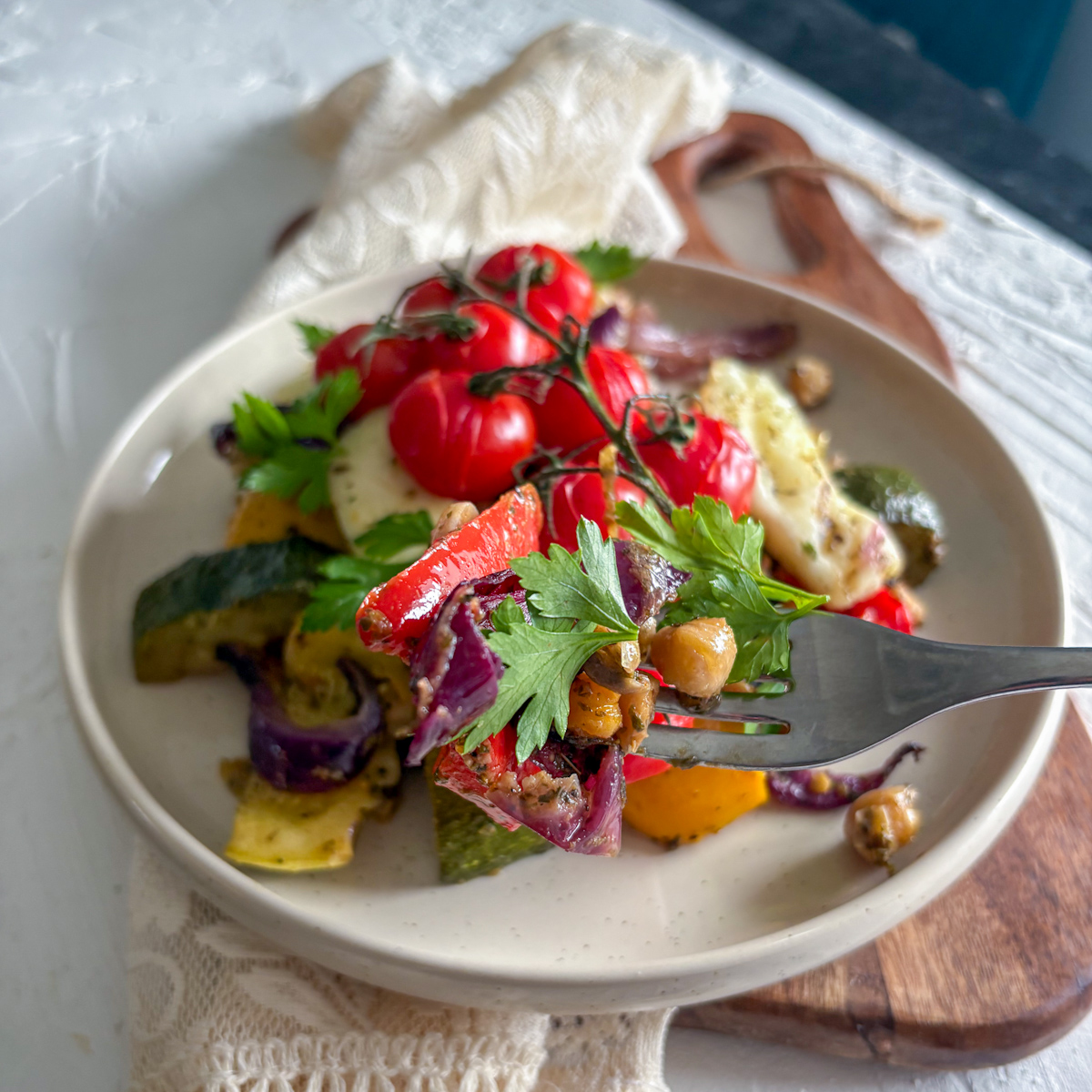 A fork lifting a bite of roasted peppers, red onion, and chickpeas from a savoury halloumi traybake.