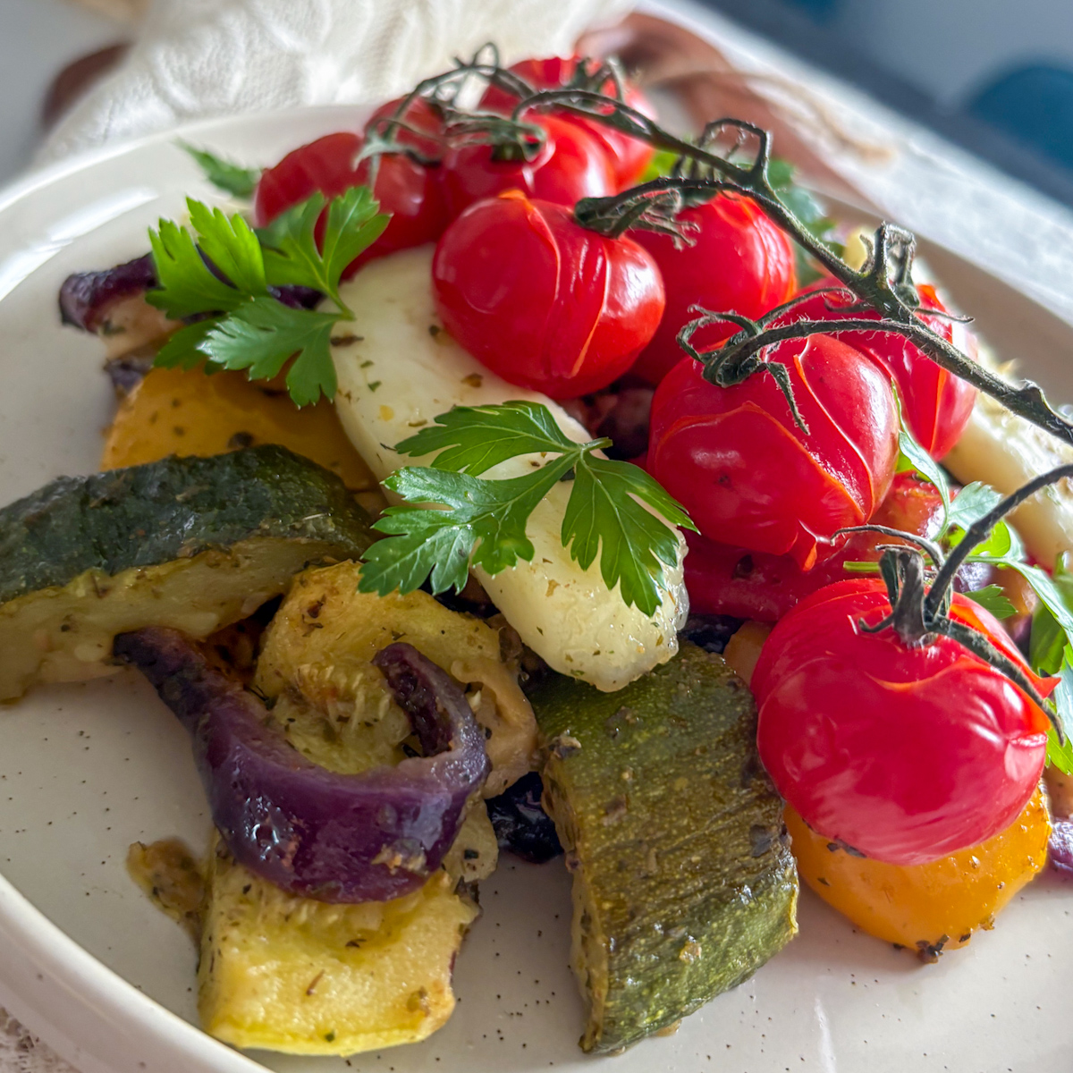 Eye-level shot of roasted vegetables and halloumi highlighting caramelised red onions and courgette wedges.