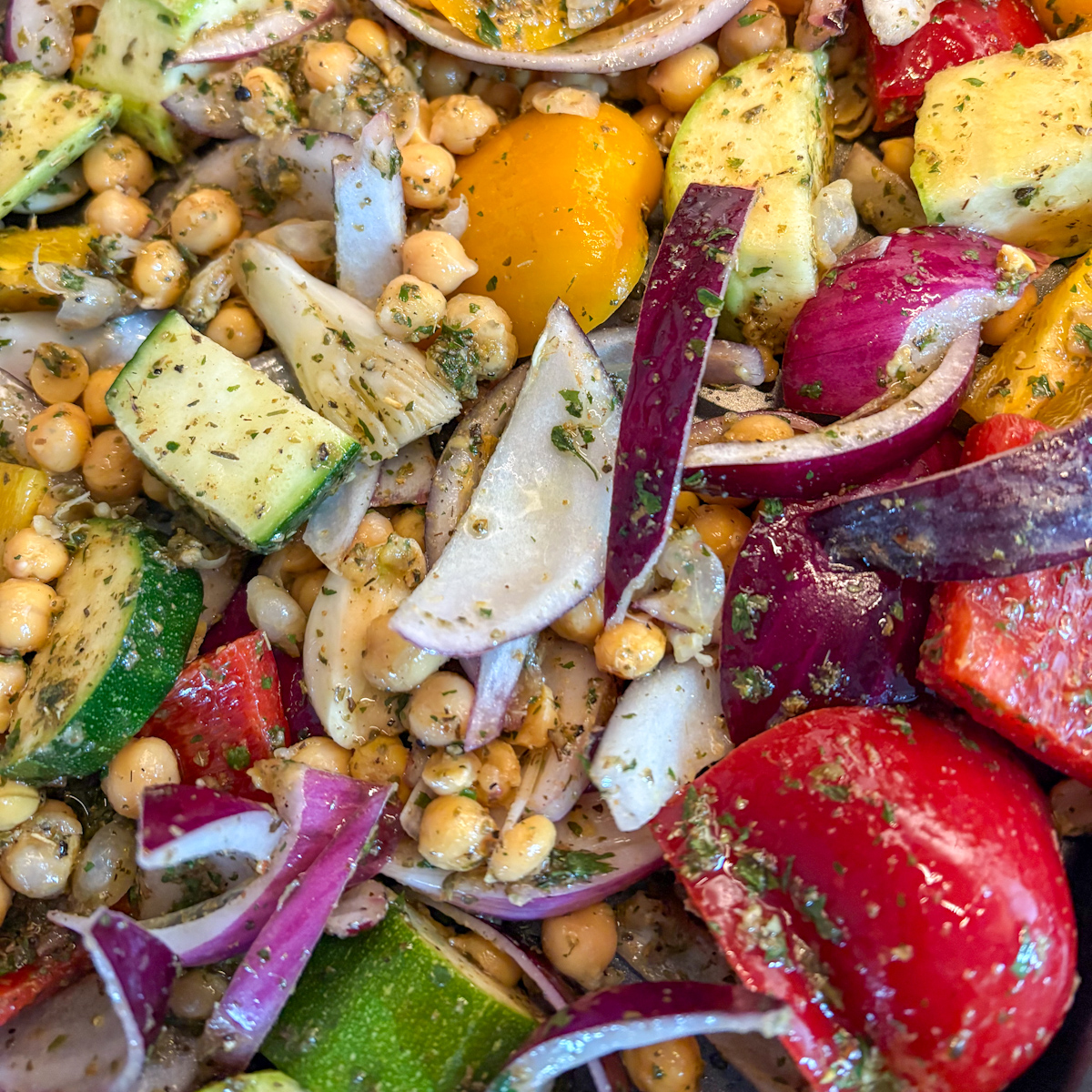 A close-up view of seasoned raw Mediterranean vegetables and chickpeas on a baking tray, prepping for our roasted vegetables and halloumi recipe.