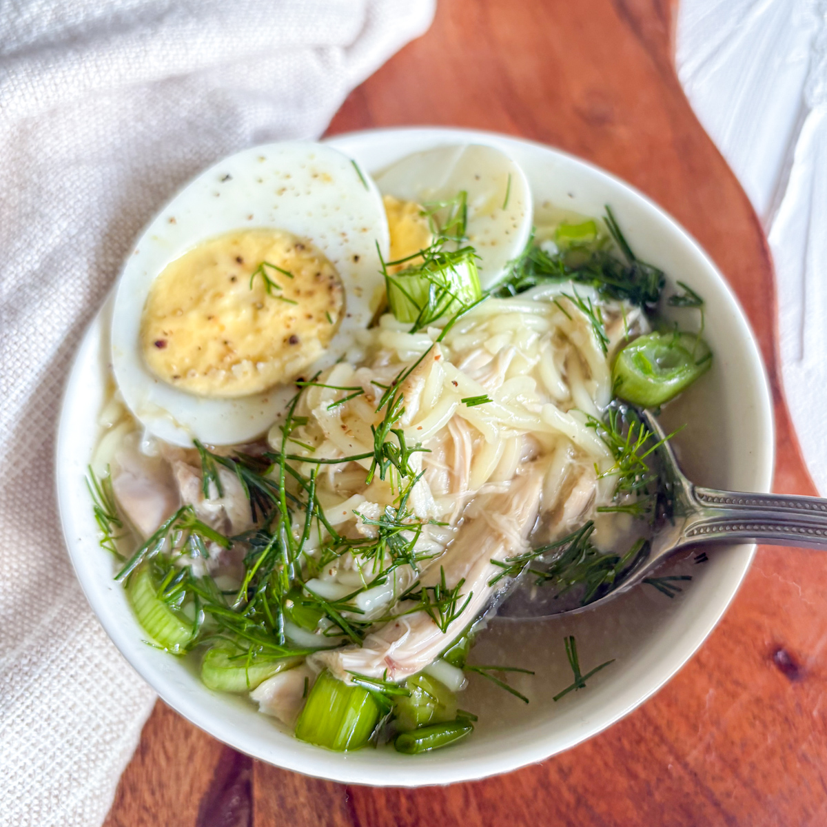 Russian chicken soup served in white bowl with fresh herbs and egg
