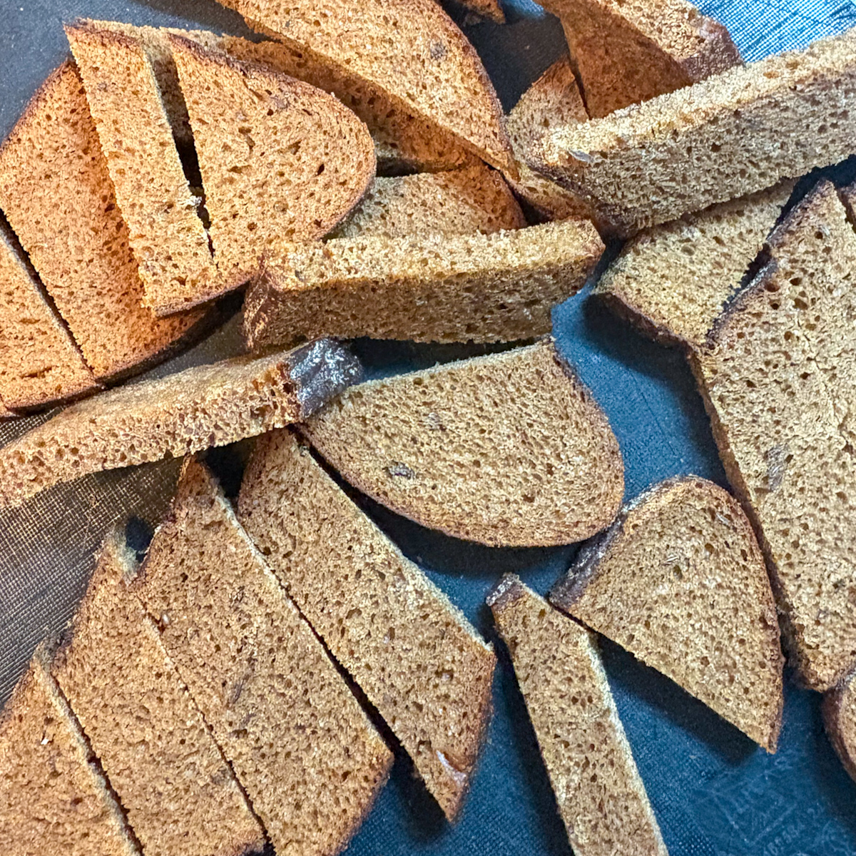 Sliced dark bread strips on a board prepared for making a Garlic grenki recipe.