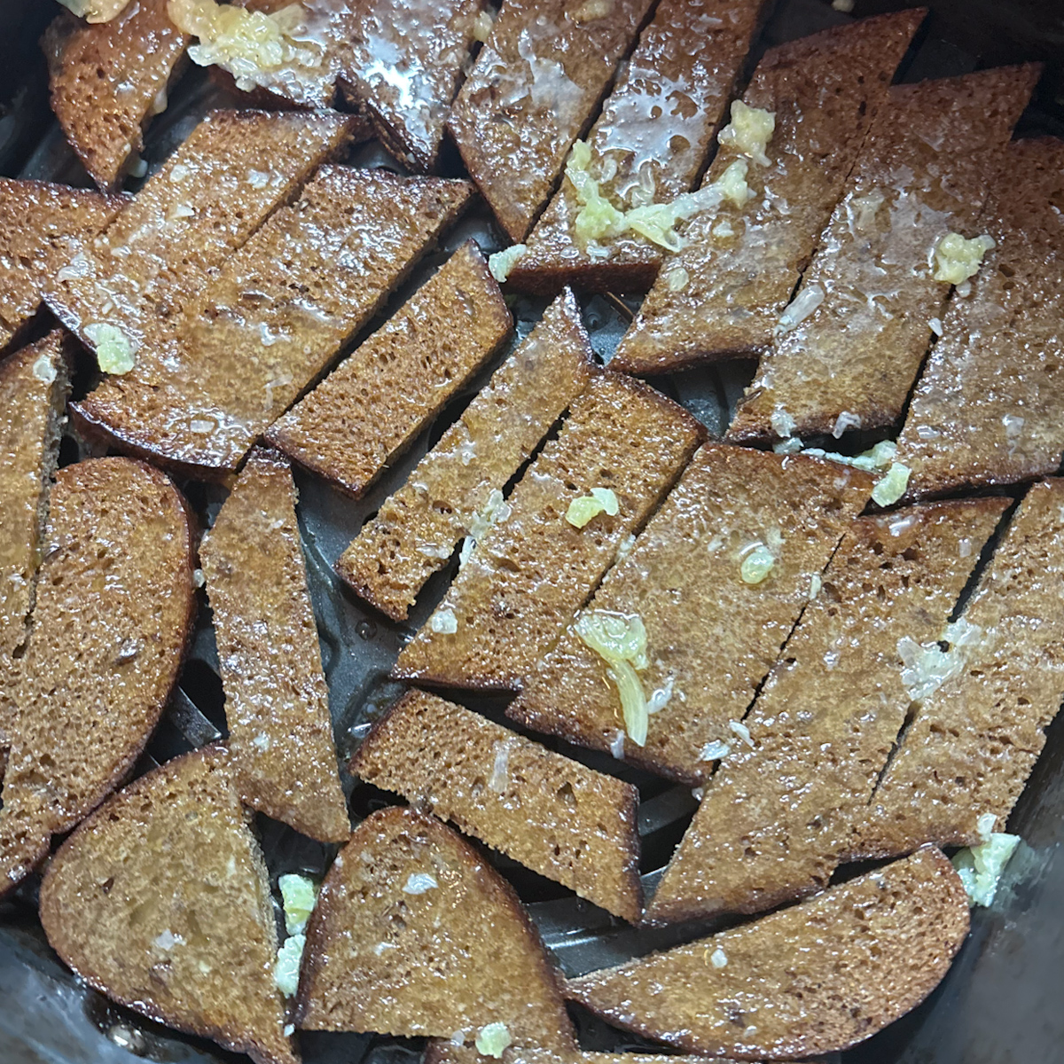 Rye bread grenki strips being roasted in a single layer inside an air fryer basket.