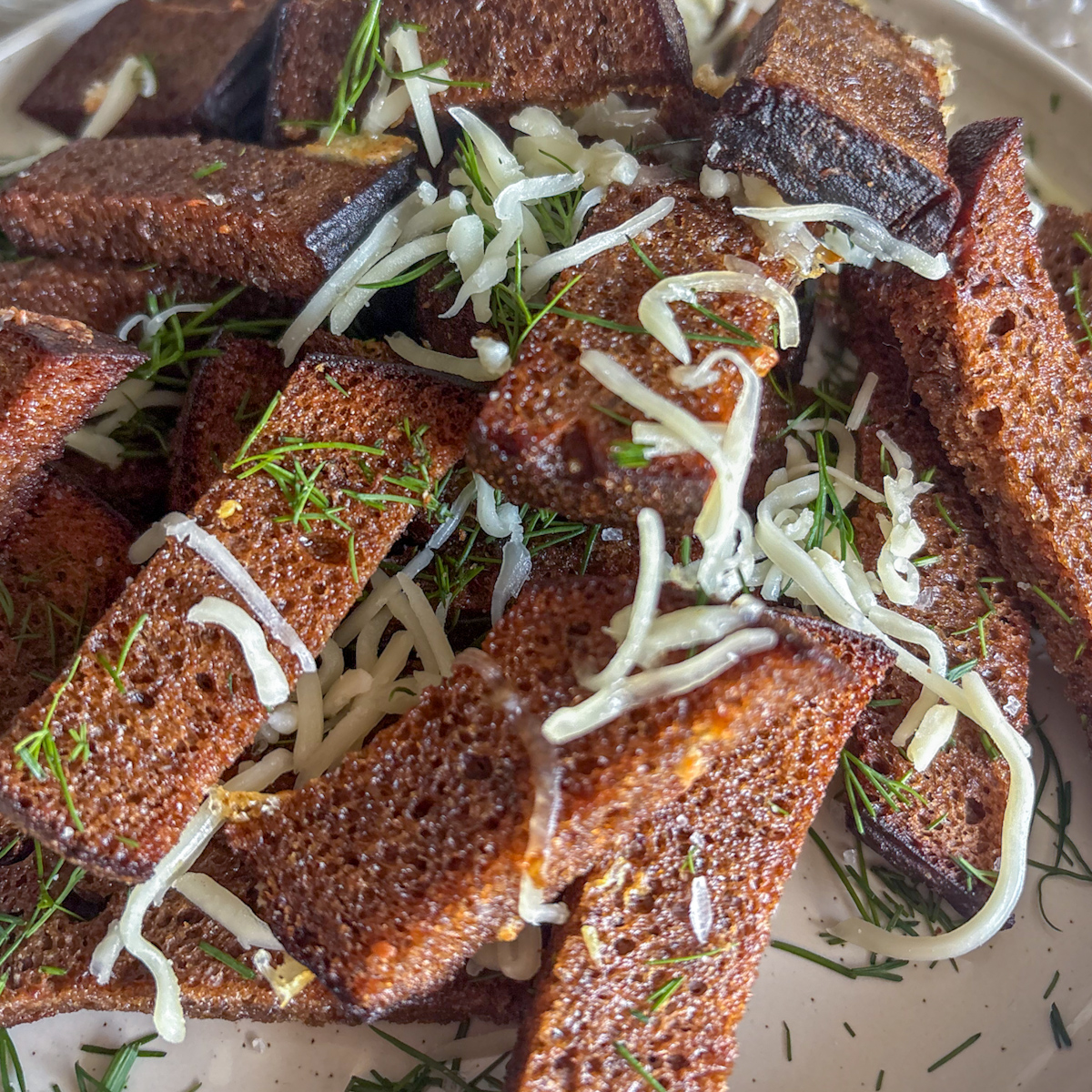 Rustic appetiser of rye bread strips garnished with fresh dill and grated mozzarella