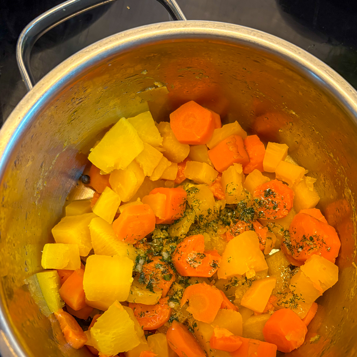Boiled turnip and carrot cubes in a pot with garlic herb butter for mash