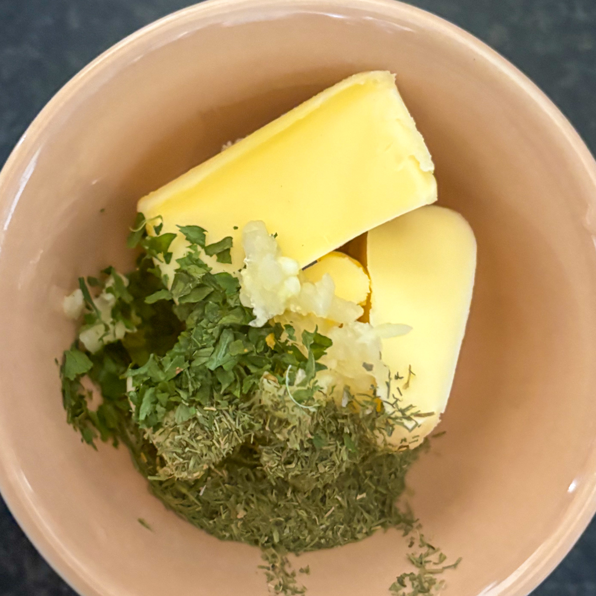 Butter, minced garlic, dried dill and parsley in a bowl for carrot and turnip mash