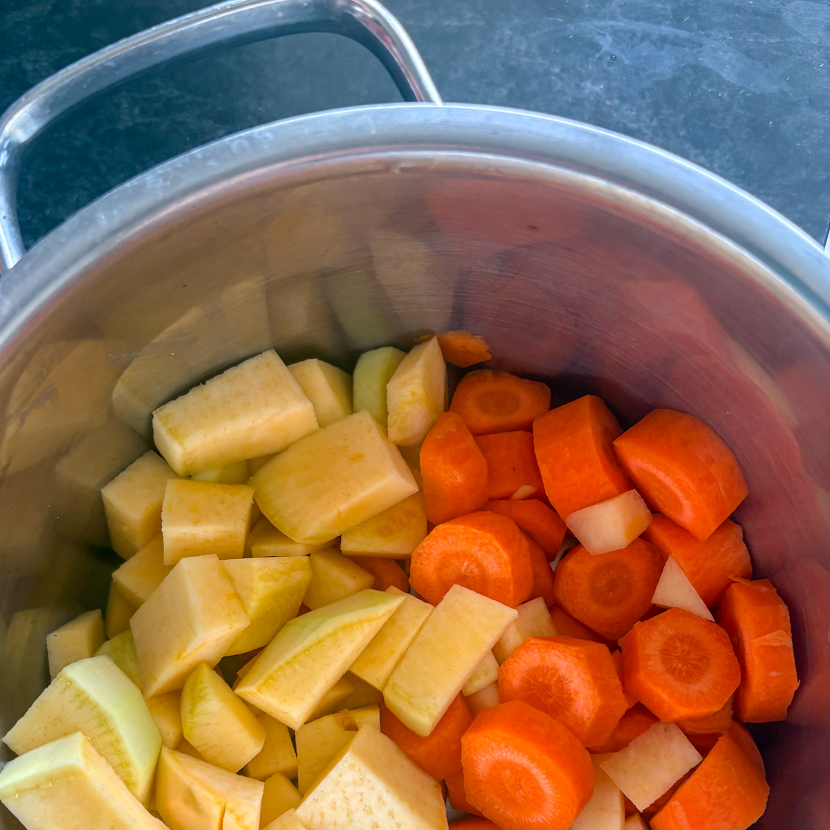 Peeled and cubed turnips and carrots in a pot ready for boiling