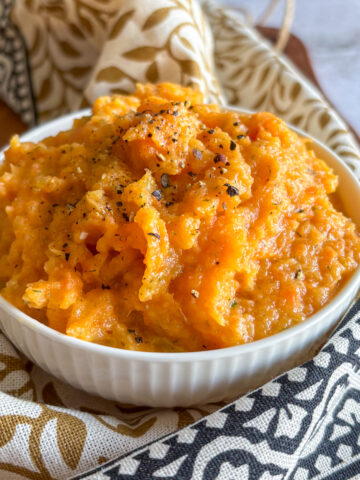 Creamy carrot and turnip mash in a white bowl topped with black pepper and herbs
