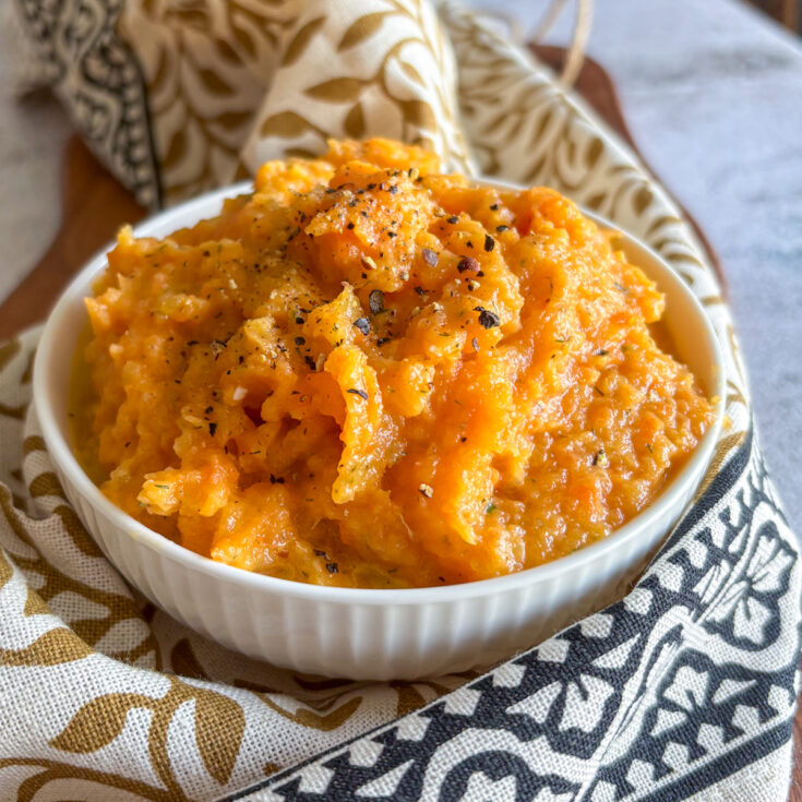 Creamy carrot and turnip mash in a white bowl topped with black pepper and herbs