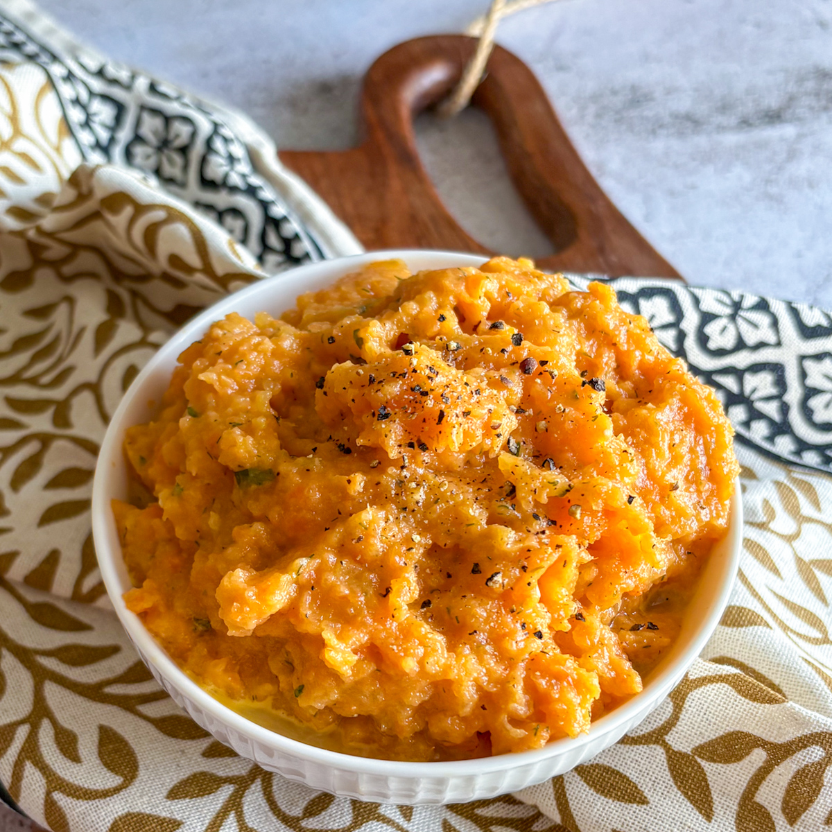 Easy carrot and turnip mash in a bowl on a patterned tea towel