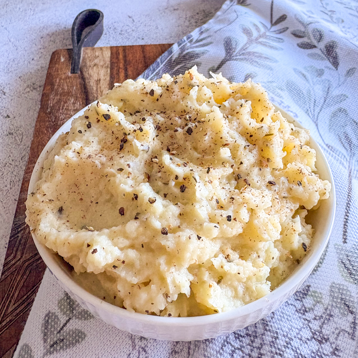 Silky mashed parsnips piled in white bowl with cracked black pepper, thyme and grated nutmeg
