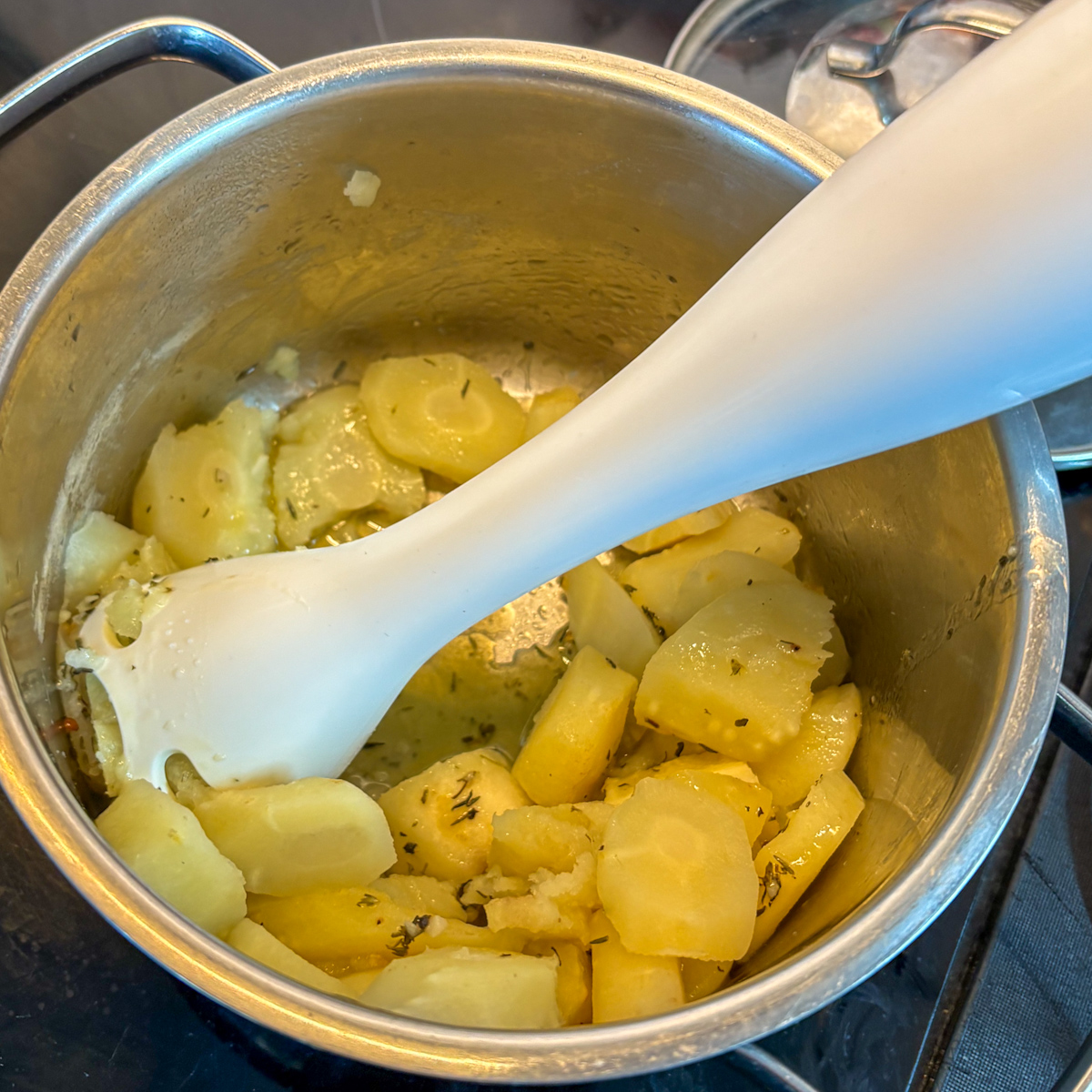 Hand blender pureeing boiled parsnips with thyme and butter in pot for creamy parsnip mash recipe