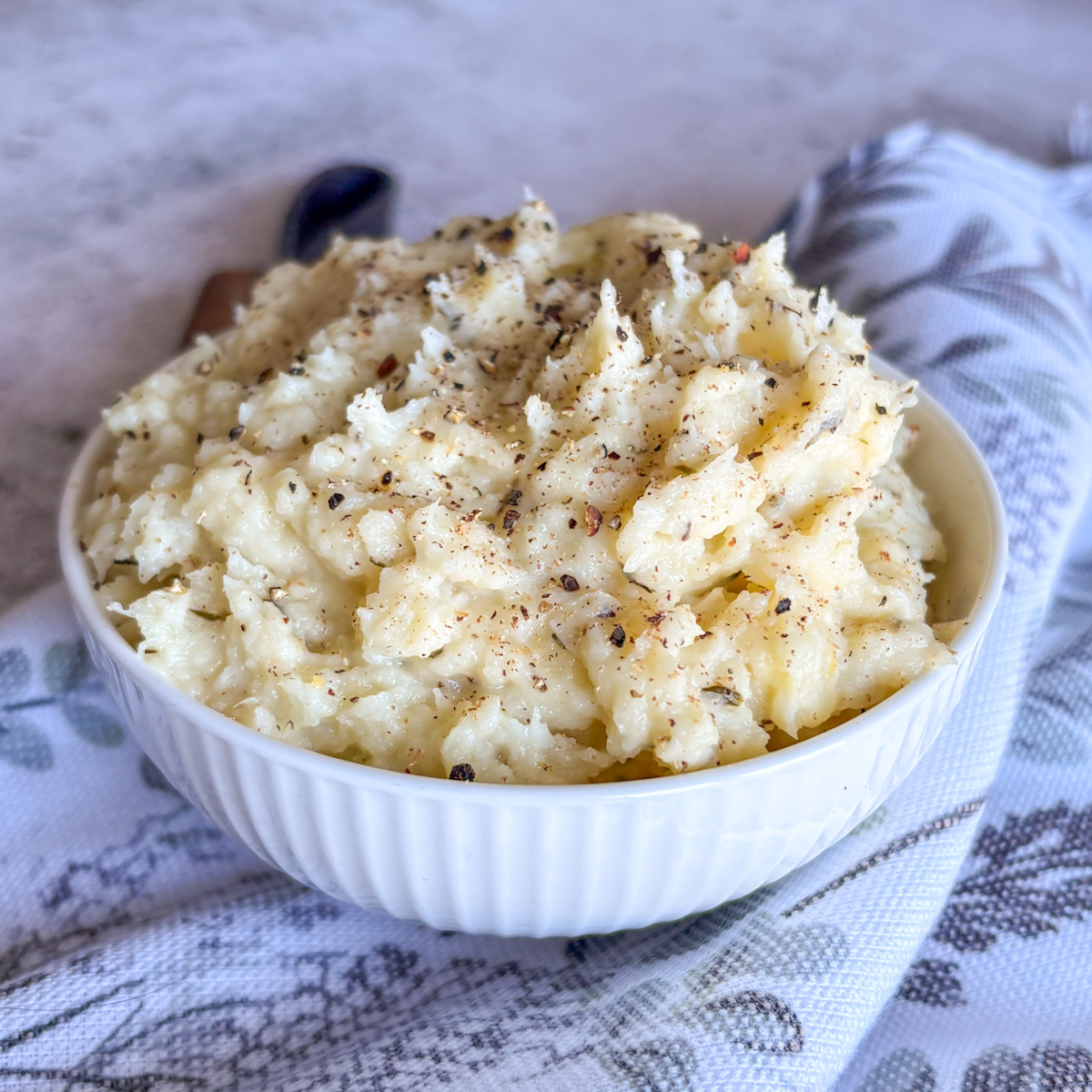 Buttery parsnip mash recipe in white bowl with black spoon and seasoned with thyme and pepper
