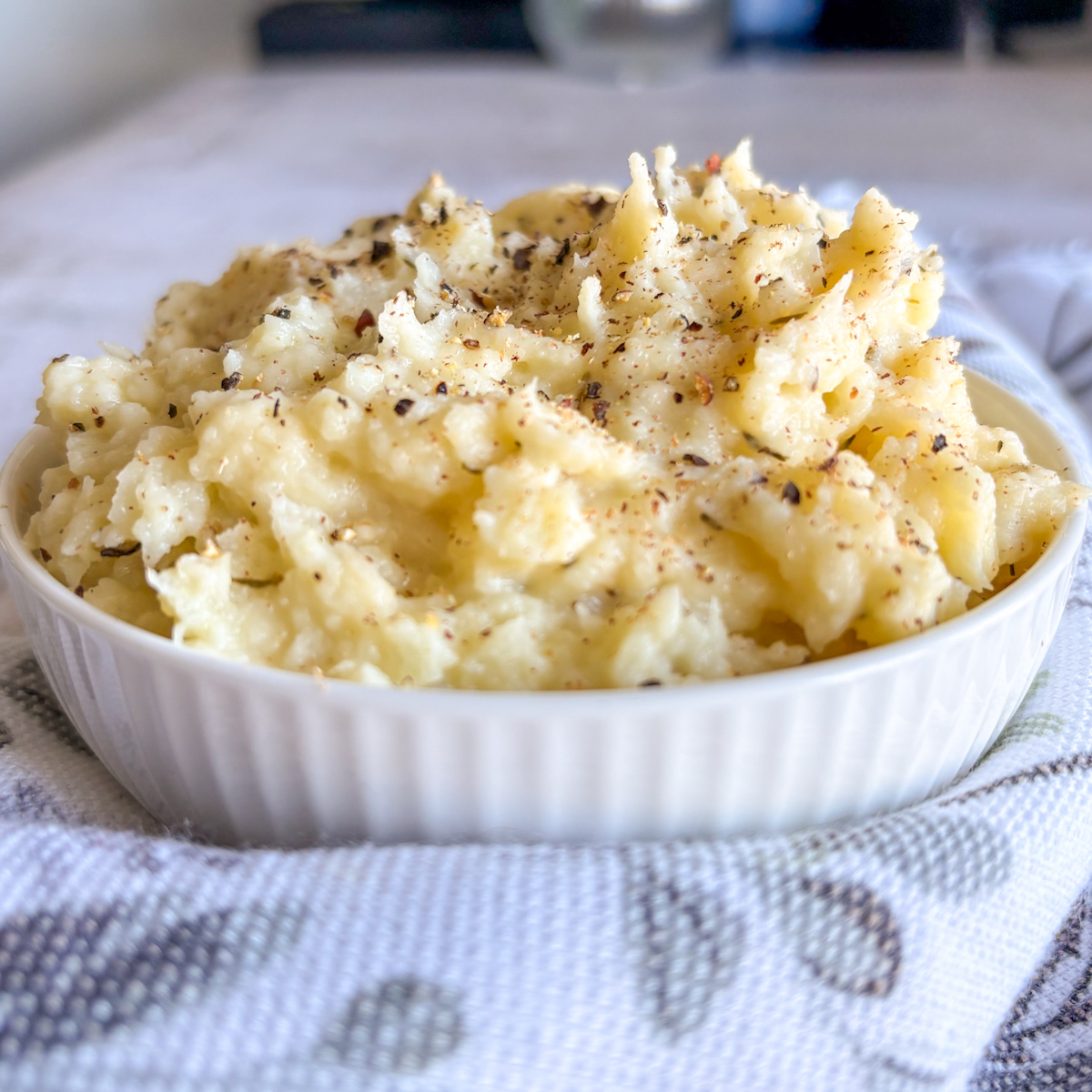 Creamy parsnip mash in white bowl topped with herbs, pepper and nutmeg, served with fork on board