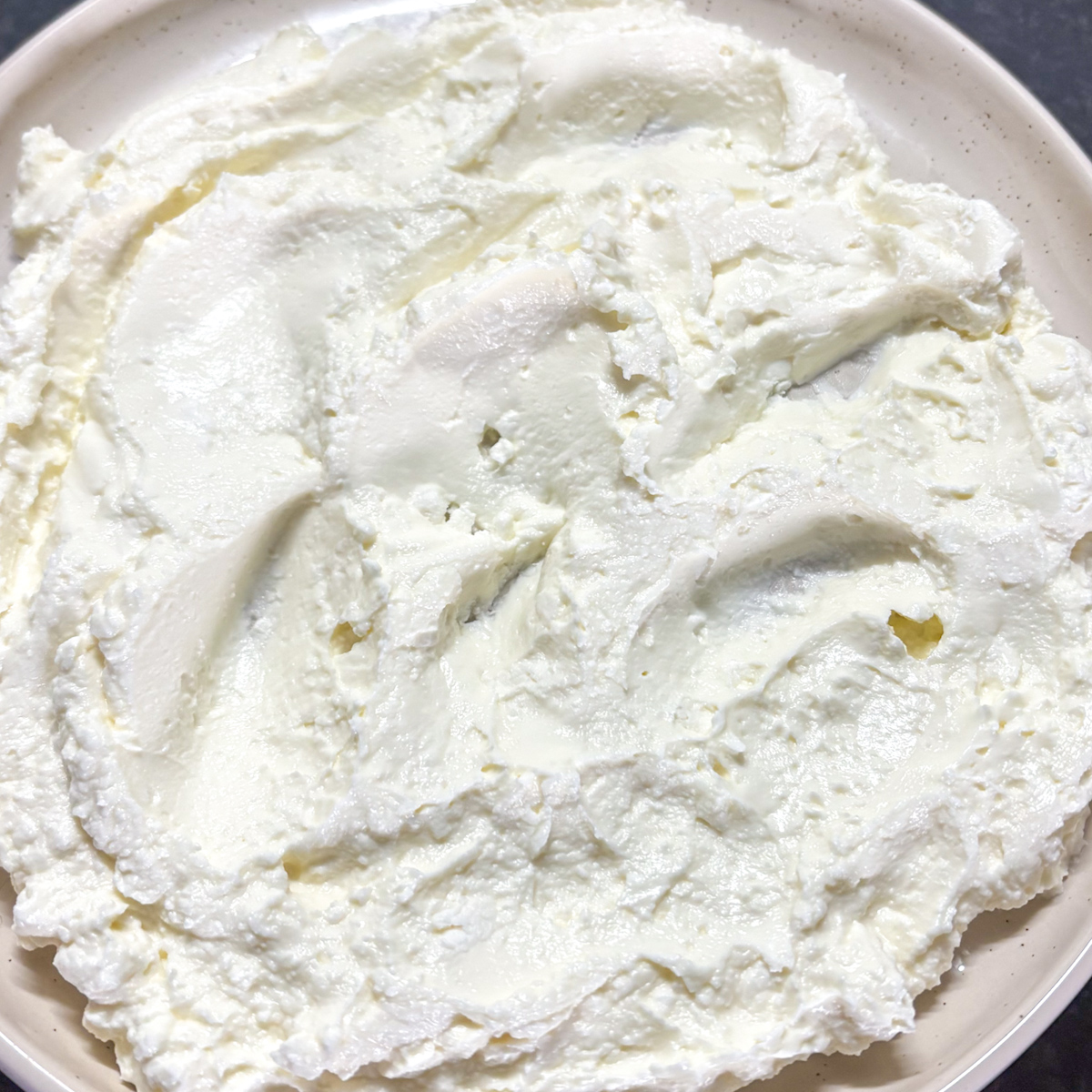 Smooth and creamy whipped feta dip spread across a ceramic plate before topping