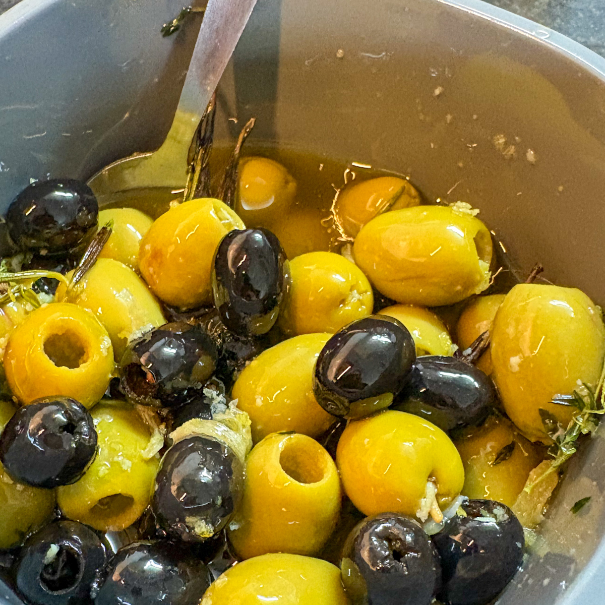 Bowl of warm marinated olives with garlic, rosemary, thyme and lemon peel in olive oil