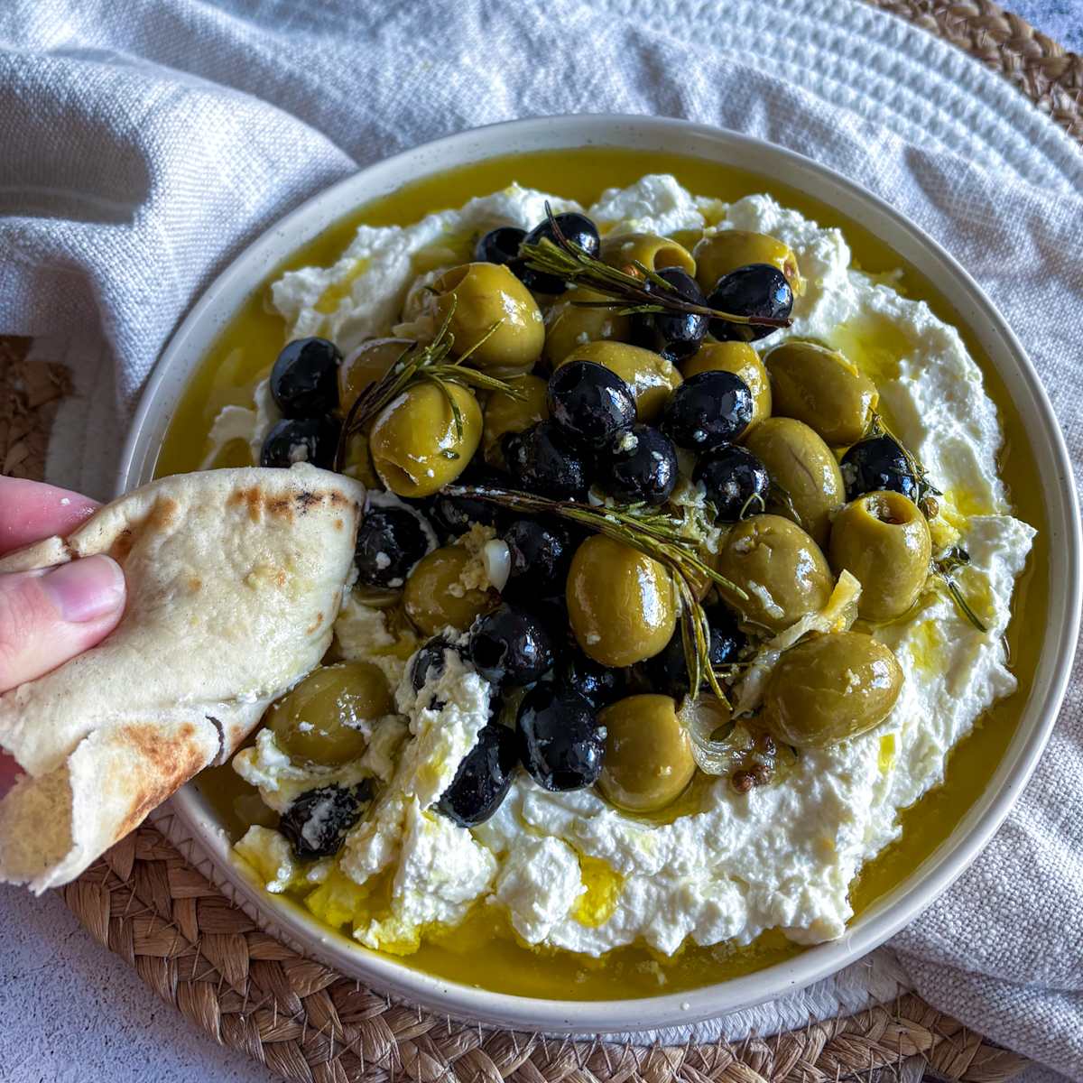 Hand dipping flatbread into marinated olives and whipped feta with rosemary and herb oil