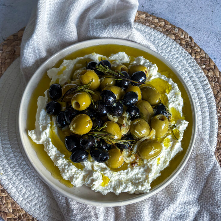Mediterranean appetiser with warm marinated olives spooned over silky whipped feta
