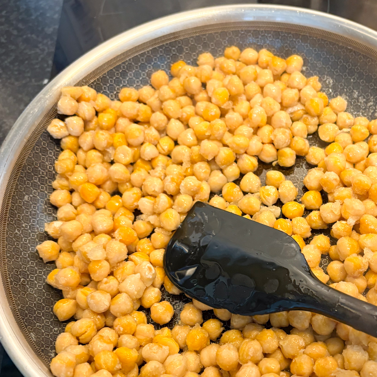 Stirring chickpeas in hot oil with a black spatula to create perfectly golden stovetop crispy chickpeas.