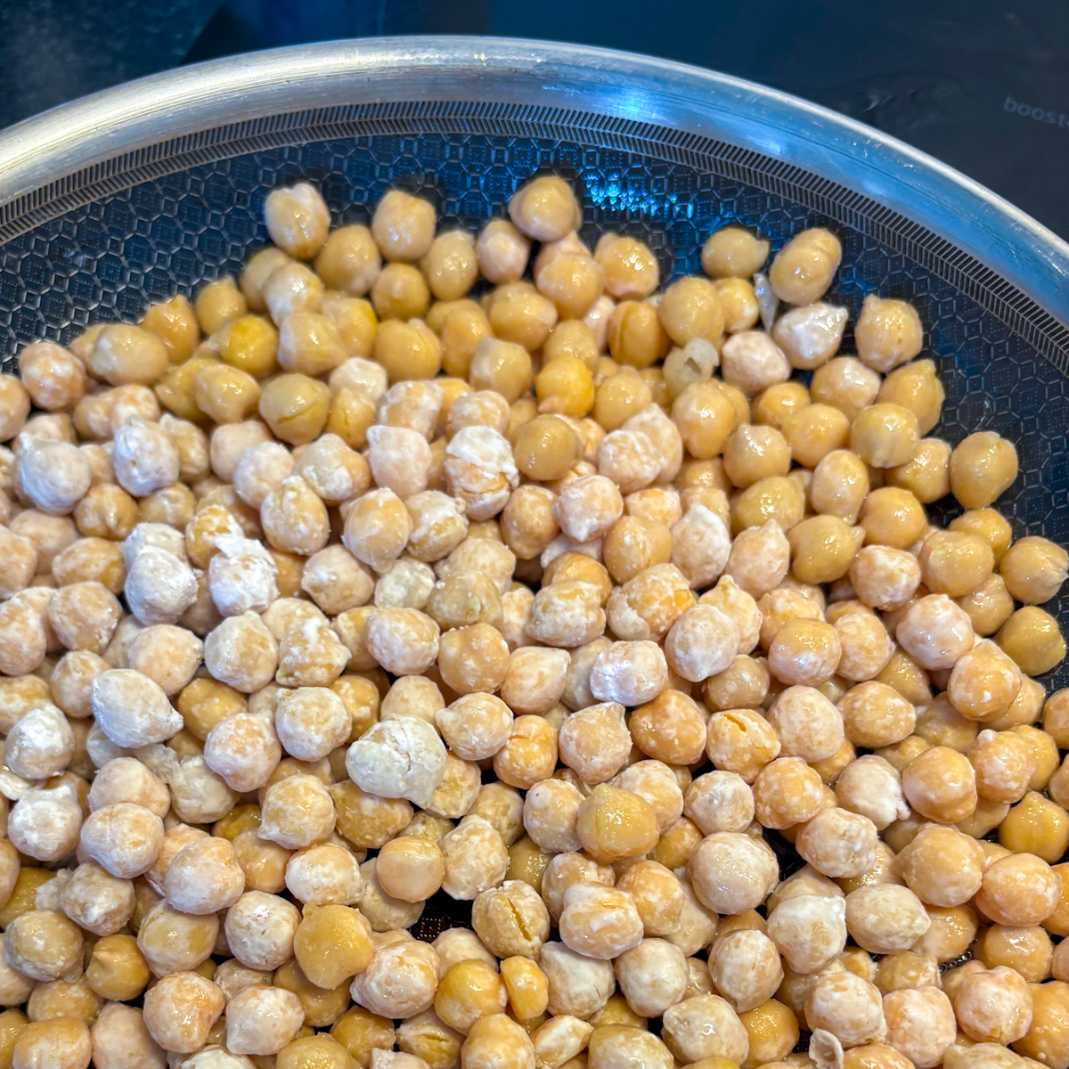 Raw chickpeas evenly coated in cornflour resting in a frying pan, ready to become a gluten-free pan-fried chickpea snack.