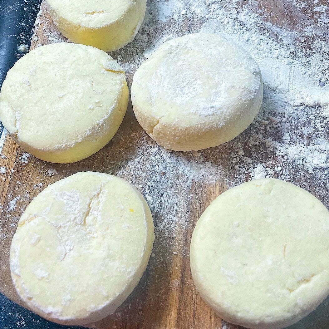 Shaped Ricotta Syrniki dough rounds dusted with flour on a wooden board before frying.